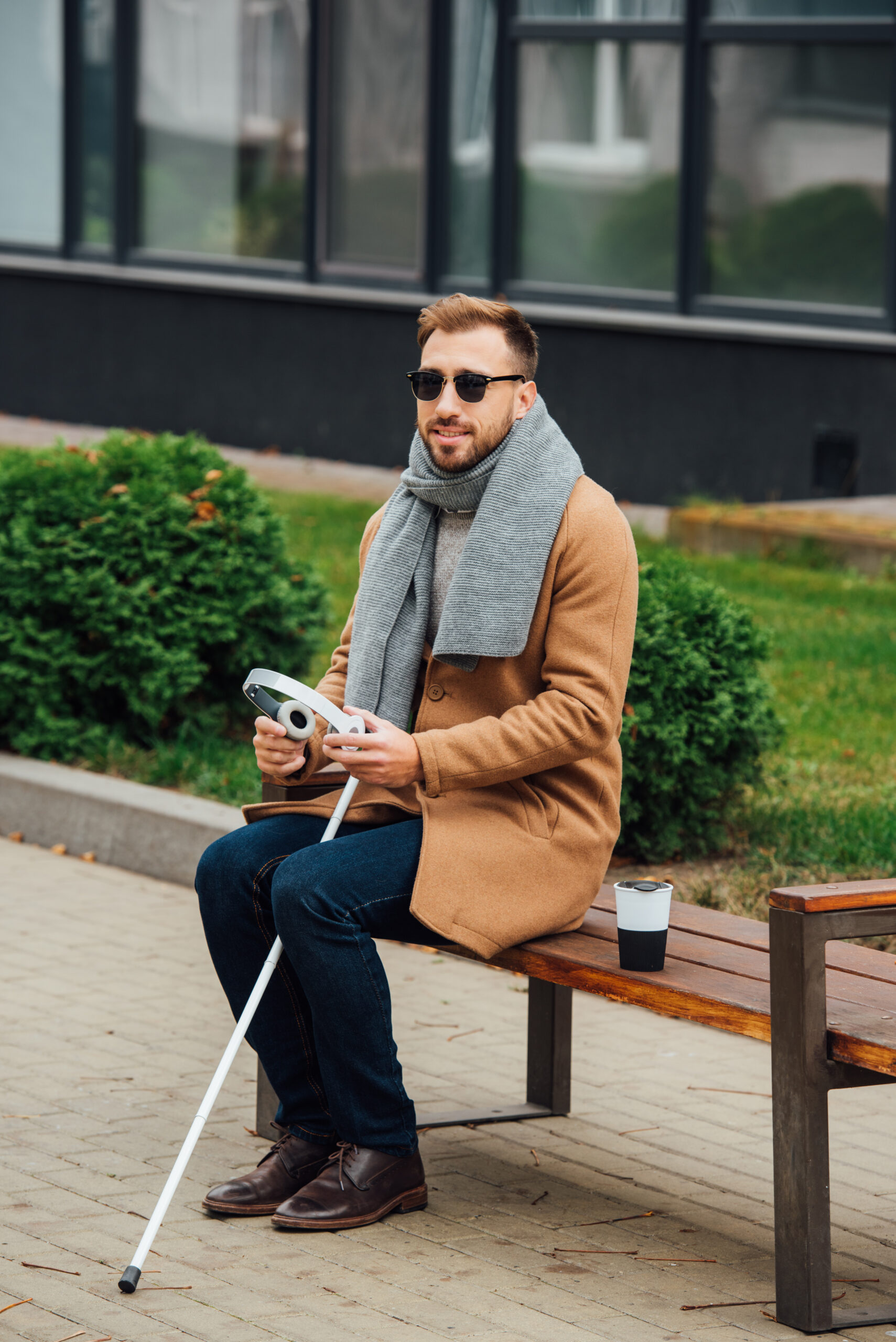 Blind man holding headphones while sitting on bench