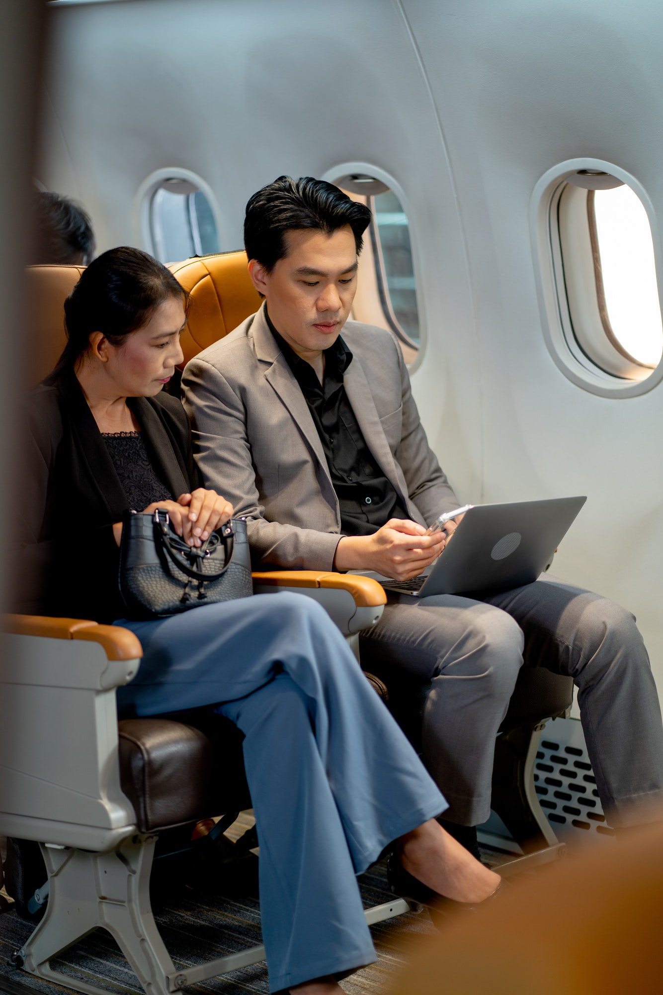 Two people sat on a plane working on a laptop