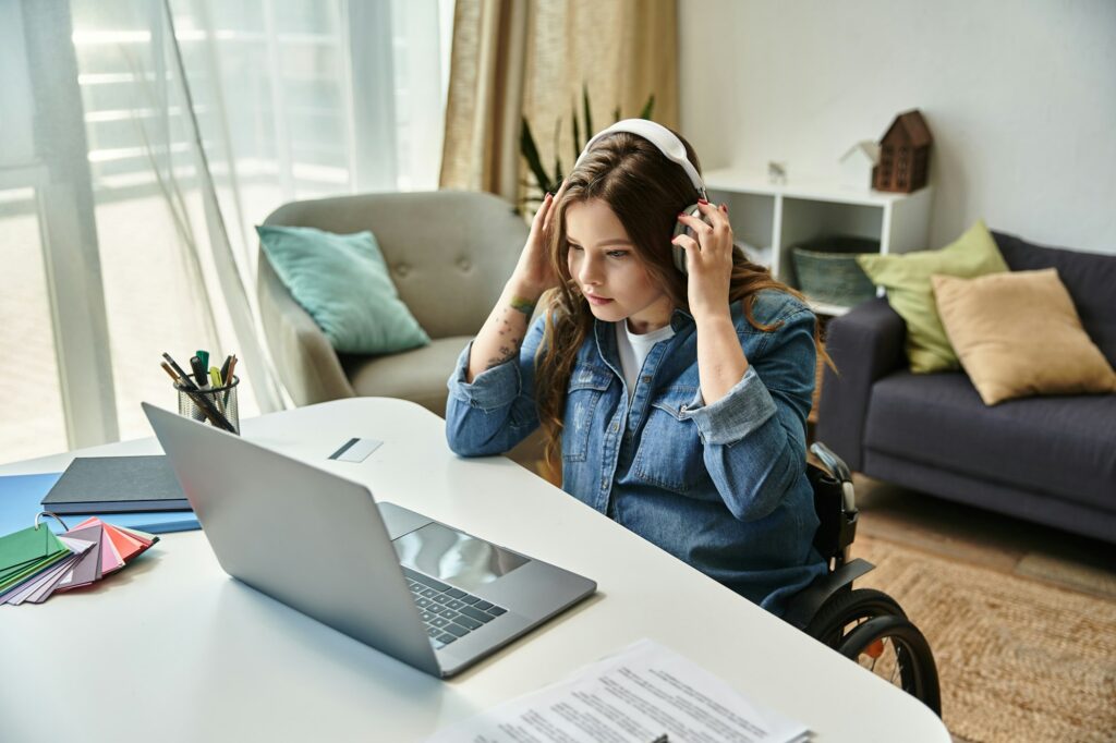 Pretty brunette woman in a wheelchair, putting on headphones, about to start a blog on her laptop