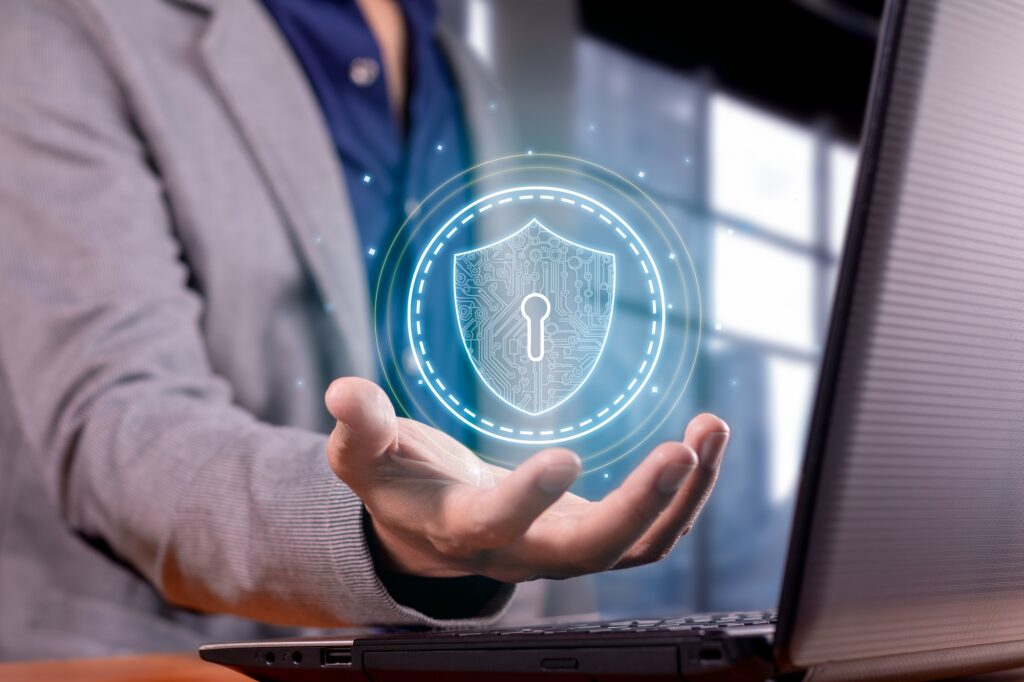 A guy in a grey jacket stood in front of a laptop. His hand is outstretched as though holding something, with a shield floating above his hand. It's showing that your cybersecurity is in your control, just like with Firefox's privacy changes.