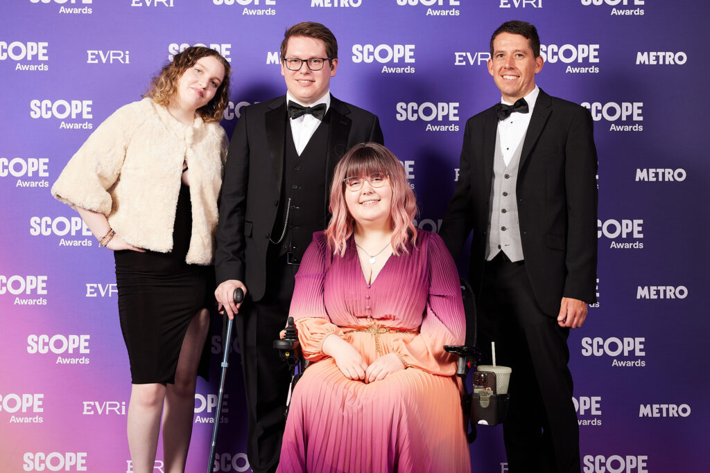 Four adults from the Inkfire Team, standing against a purple background which reads 'Scope' and 'Metro'. They're smiling, with one woman towards the front in a wheelchair.