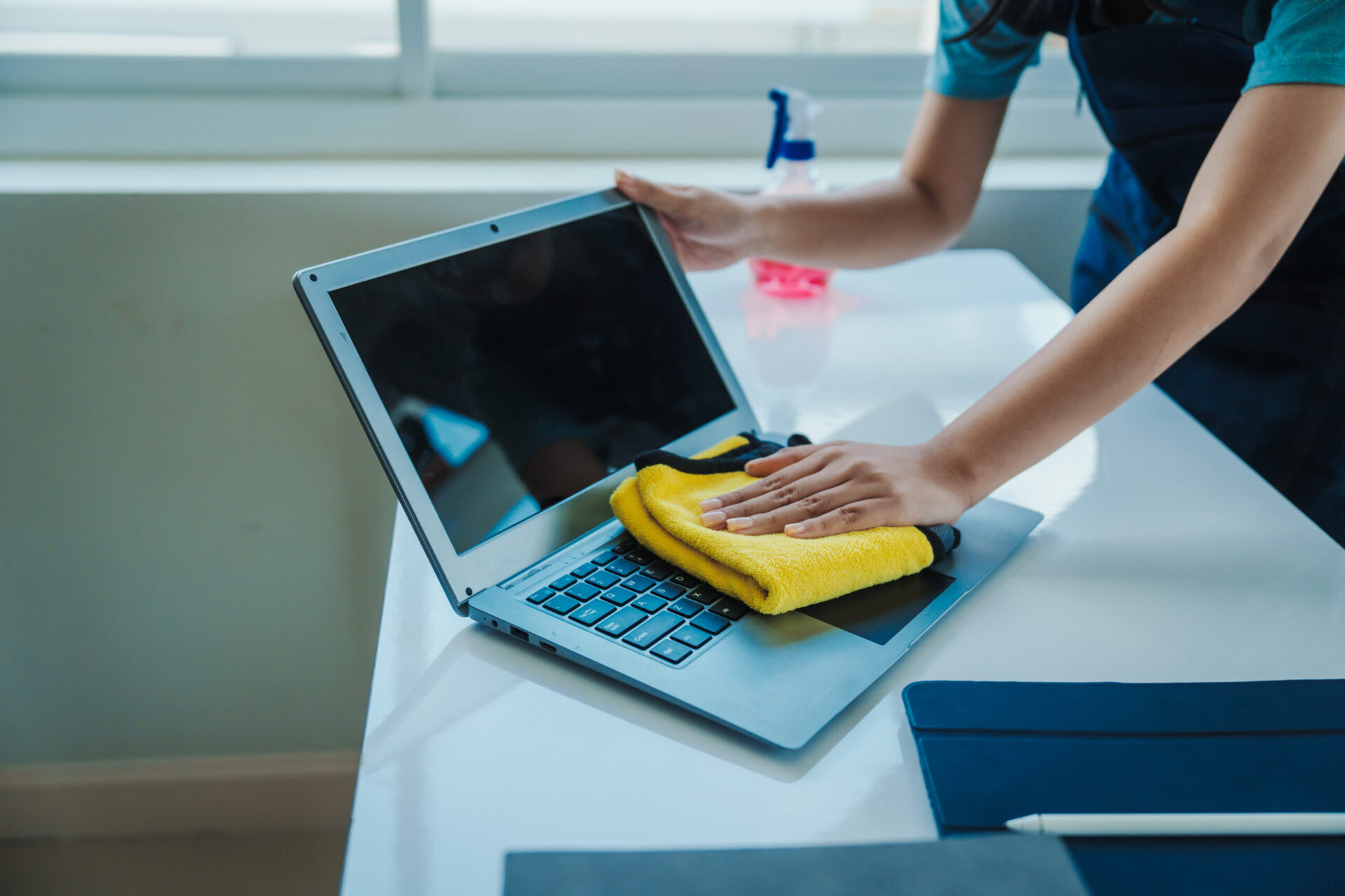 Hands cleaning a laptop keyboard.