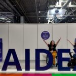 A blue text photospot at Naidex, with the words 'Naidex'. Behind the letters sit two wheelchair users, with their hands in the air.